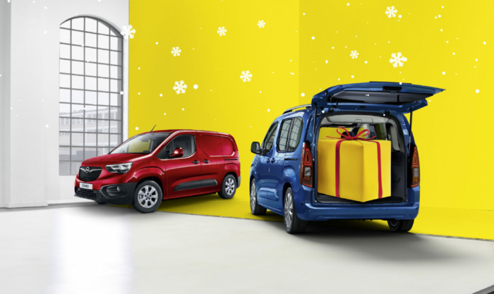 Zwei Opel-Fahrzeuge vor einer gelben Winterkulisse mit Schneeflocken; ein blauer Hochdachkombi mit geöffnetem Kofferraum, darin ein großes Geschenkpaket.