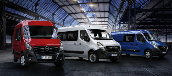 Drei Opel Nutzfahrzeuge (rot, silber, blau) in einer modernen Industriehalle bei Nacht.
