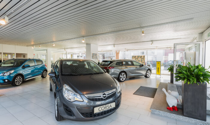 Innenansicht eines Autohauses mit mehreren ausgestellten Fahrzeugen, darunter ein Opel Corsa, im hellen und modernen Verkaufsraum.